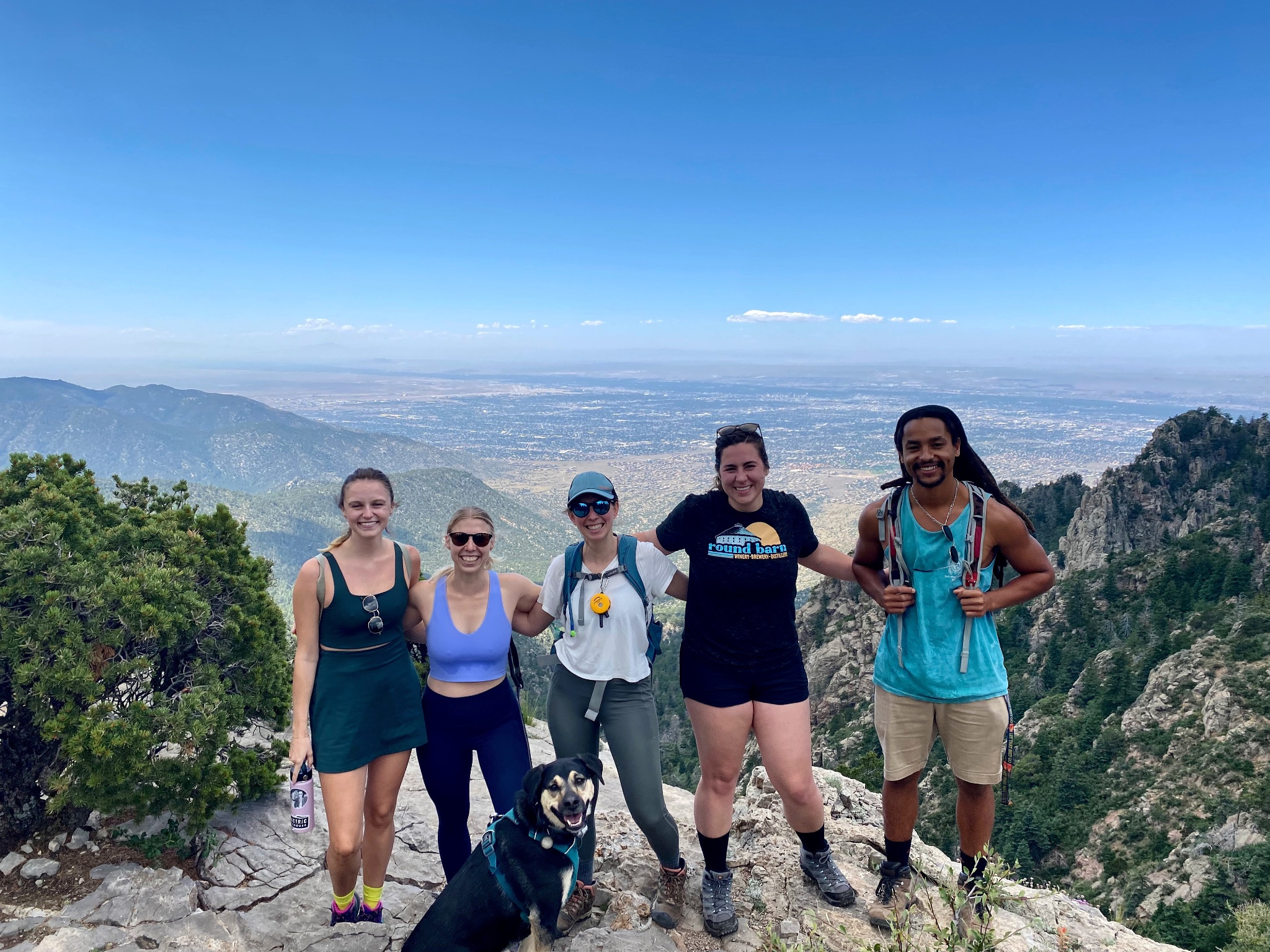 Five people and one dog on the top of a mountain with ALbuquerque behind