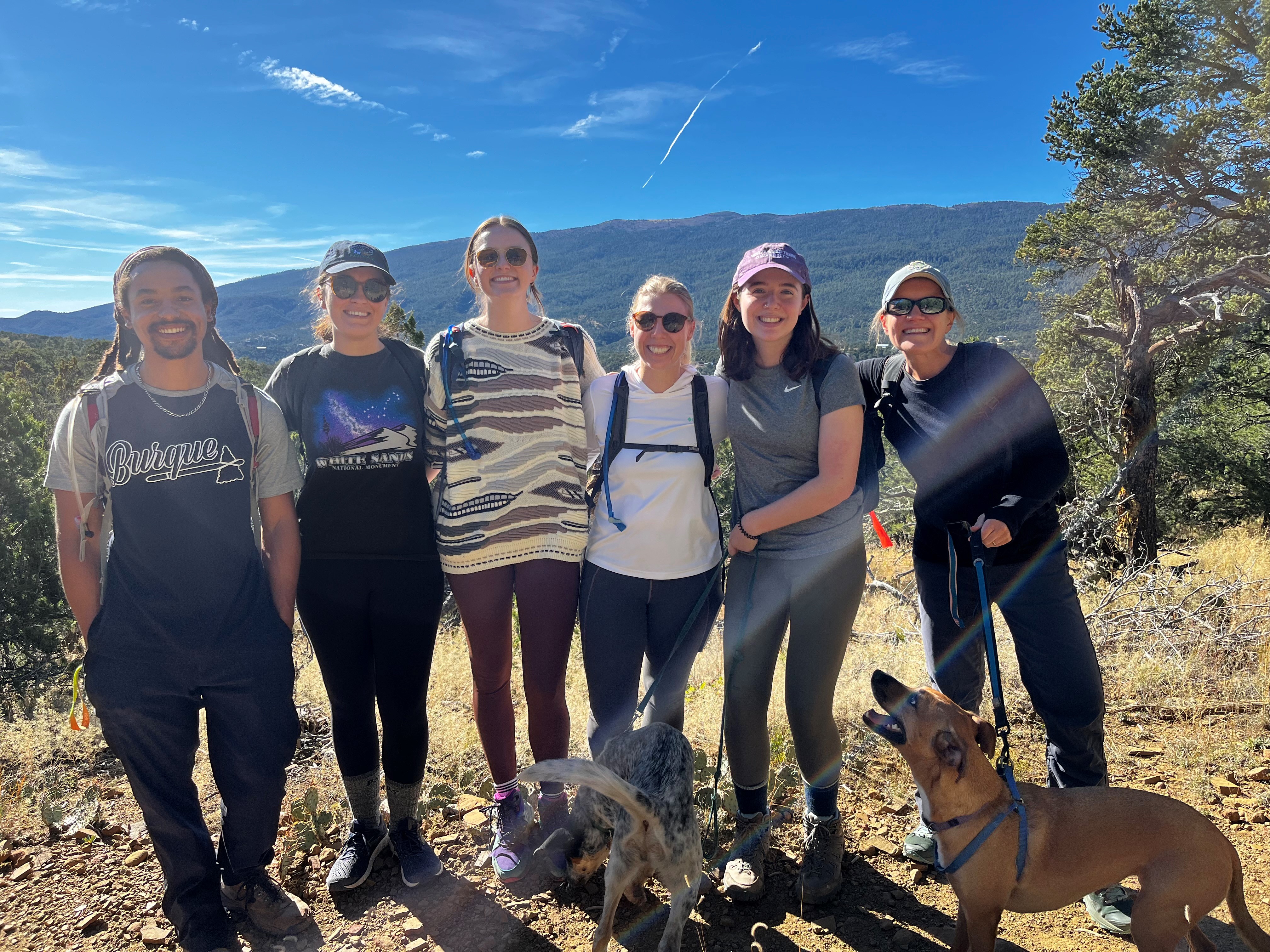 Six people and two dogs with mountains behind